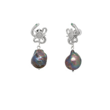 Pair of earrings with serpent design and black pearl on a white background