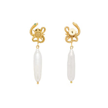 Gold serpent shaped earrings with a pearl on a light beige background