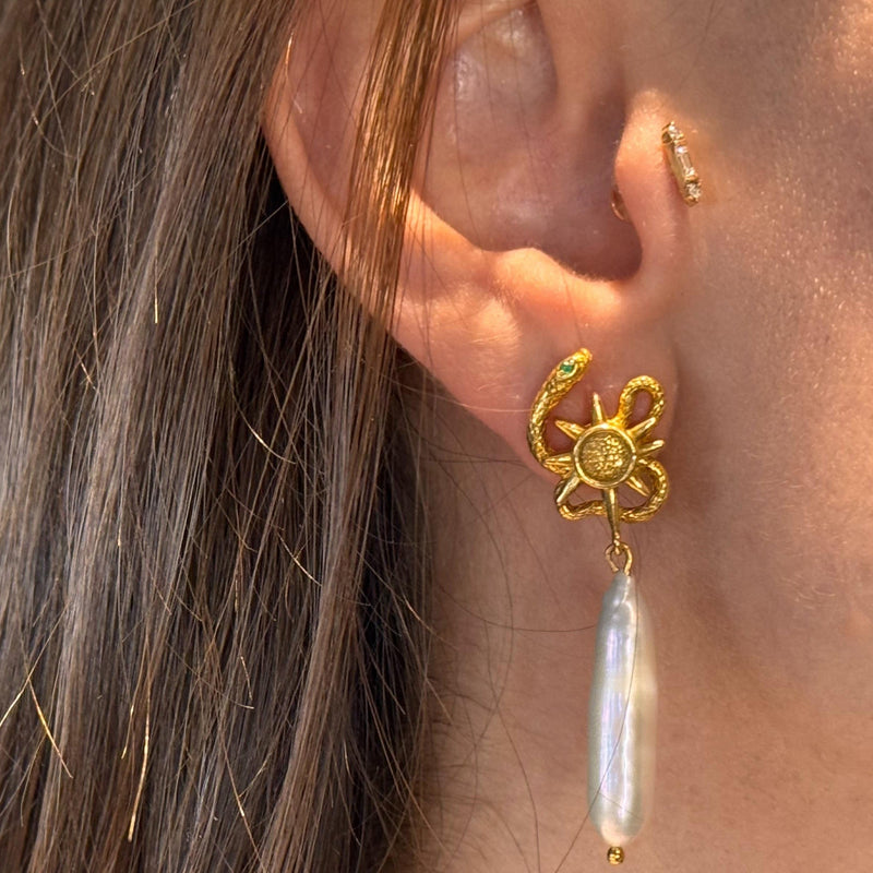 Gold serpent earring with a pearl drop worn by a person with brown hair.