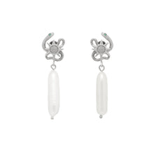 Pair of silver serpent sun design earrings with pearl on a light gray background
