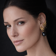 Close-up of a woman wearing gold and black earrings against a dark background