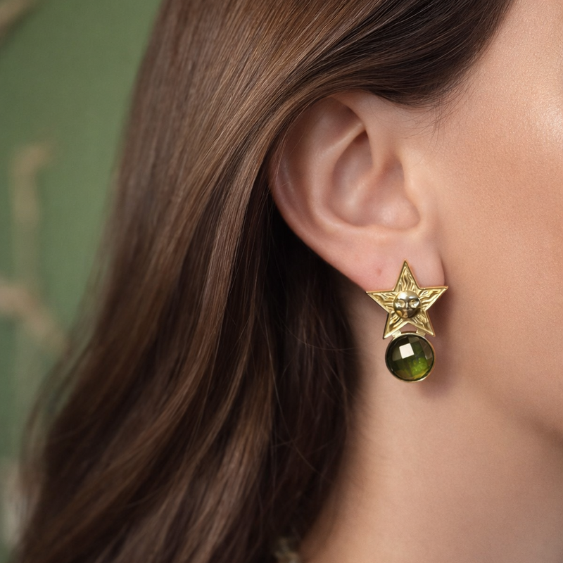 Close-up of a person wearing a gold earring with a green gemstone.
